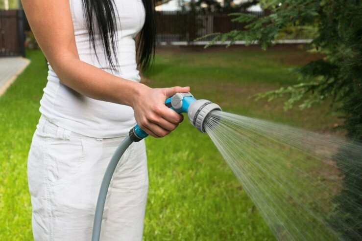 Osoba używa zraszacza pistoletowego Cellfast MIX IDEAL do nawadniania ogrodu, pokazując jednoręczną regulację strumienia wody